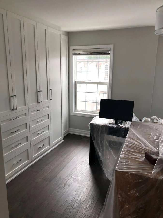 home office with built-in white cabinets and desk covered in plastic