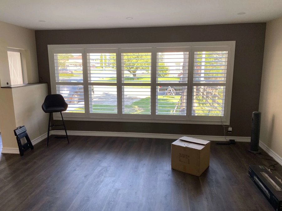 large front window with white shutters in empty room with dark flooring