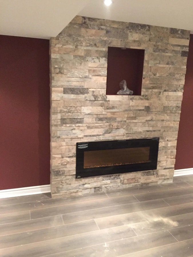 Renovated basement wall with stacked stone design, built-in electric fireplace, and display niche on deep red accent wall