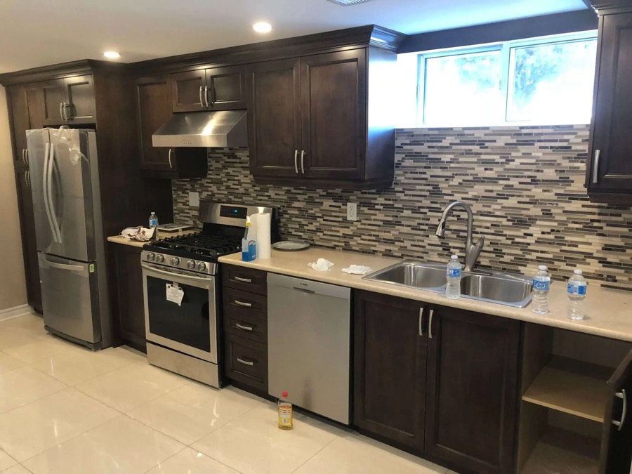 Renovated basement kitchen featuring stainless steel appliances, dark wood cabinetry, and a modern mosaic backsplash with under-window lighting