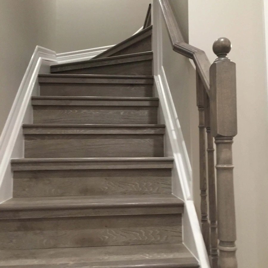 Upgraded basement staircase featuring grey-stained wood steps, white risers, and a modern wood handrail with matching post and trim
