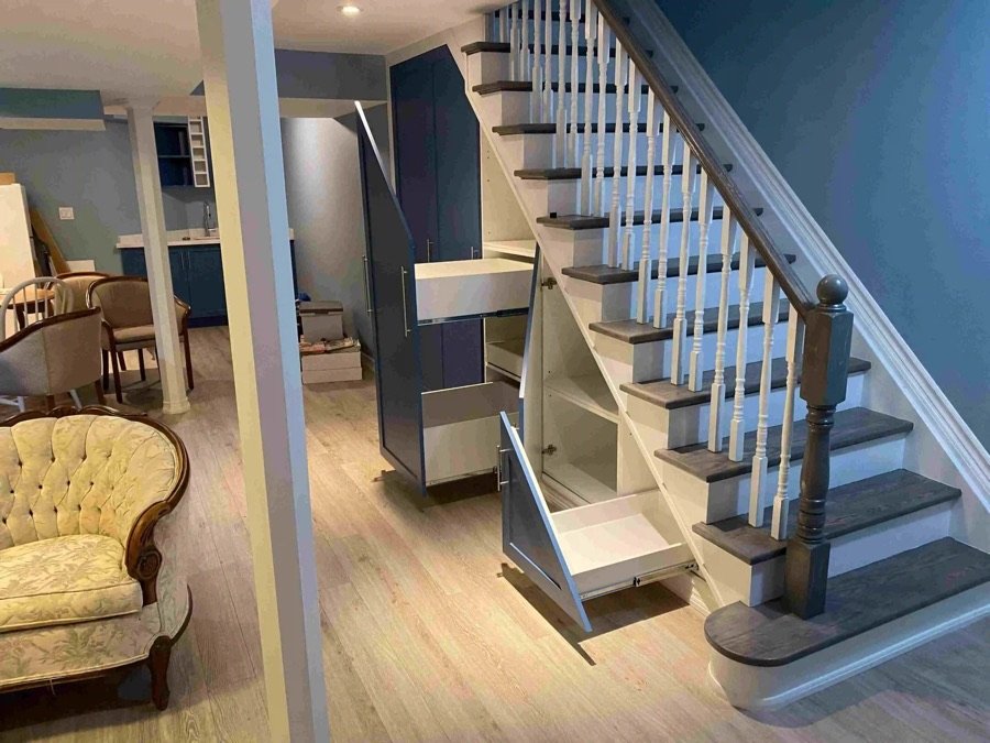 Finished basement with custom built-in drawers and cabinets under staircase, featuring modern blue cabinetry and light wood flooring