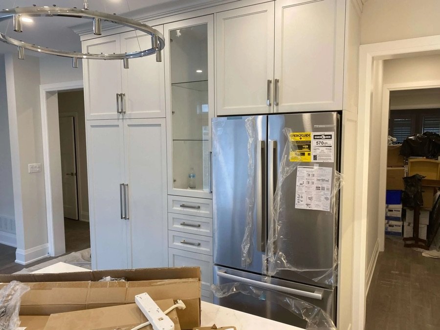 Modern kitchen renovation featuring white built-in cabinets and newly installed stainless steel fridge with energy guide label