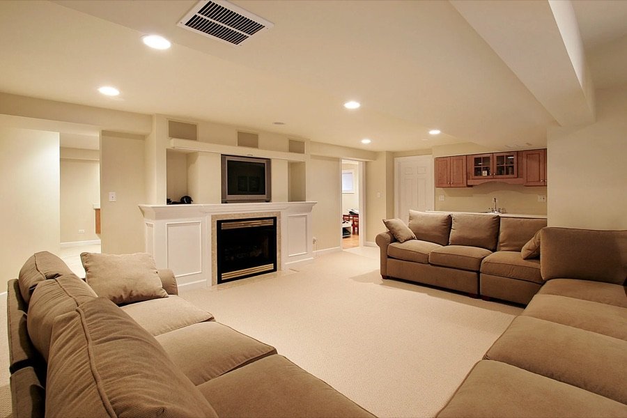 Spacious renovated basement featuring built-in fireplace, entertainment centre, cozy sectional seating, and mini bar with upper cabinets