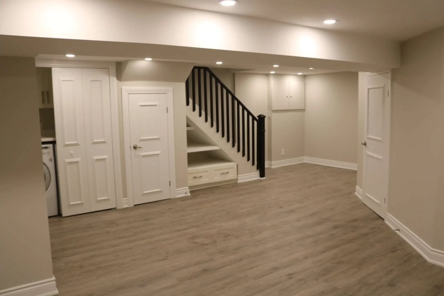 Renovated basement featuring wood-look vinyl flooring, built-in storage under stairs, recessed lighting, and laundry area closet