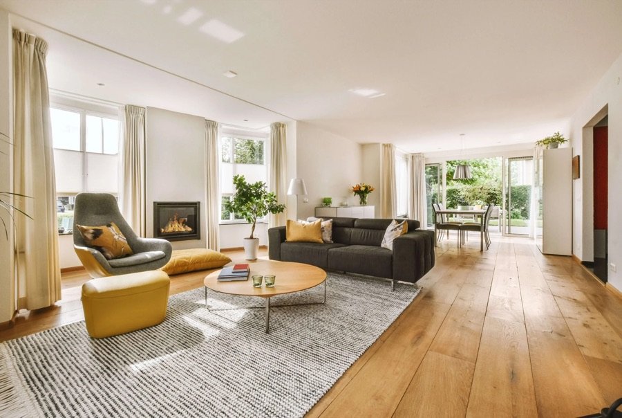 Renovated living room with light wood flooring, open layout, modern furniture, and large windows allowing natural sunlight to fill the space