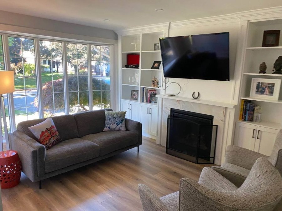 bright living room with large windows wall-mounted TV fireplace built-in shelves and gray sofa