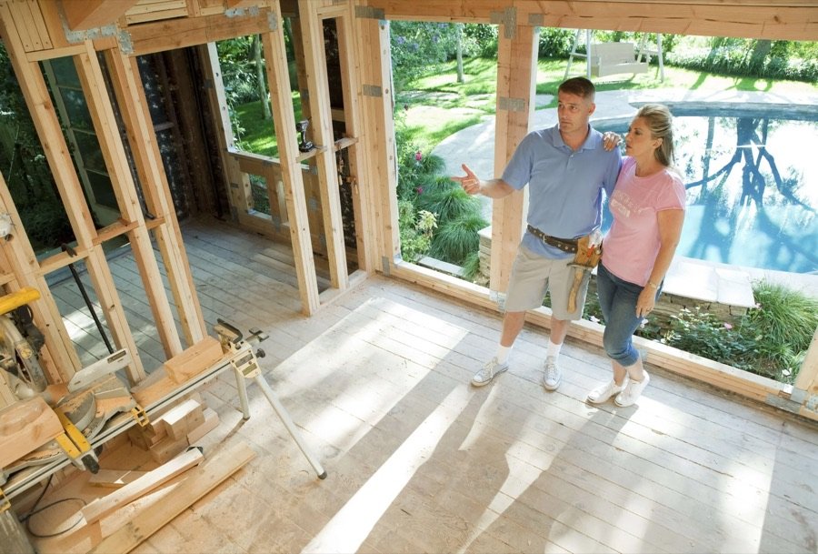 Contractor and homeowner standing in a partially framed room addition, reviewing interior layout and construction details with garden and pool in view