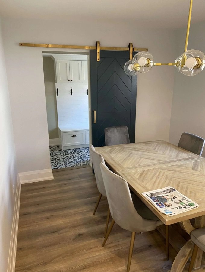 Dining area with light wood flooring and view of a dark sliding barn door leading to a white mudroom with patterned tile floor in Ontario home renovation