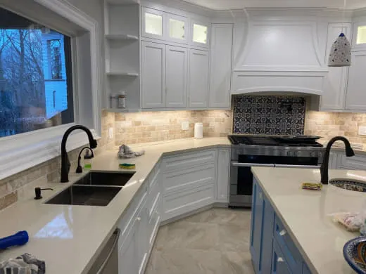 Renovated kitchen featuring white cabinets, black fixtures, tiled backsplash, and a blue centre island with quartz countertops