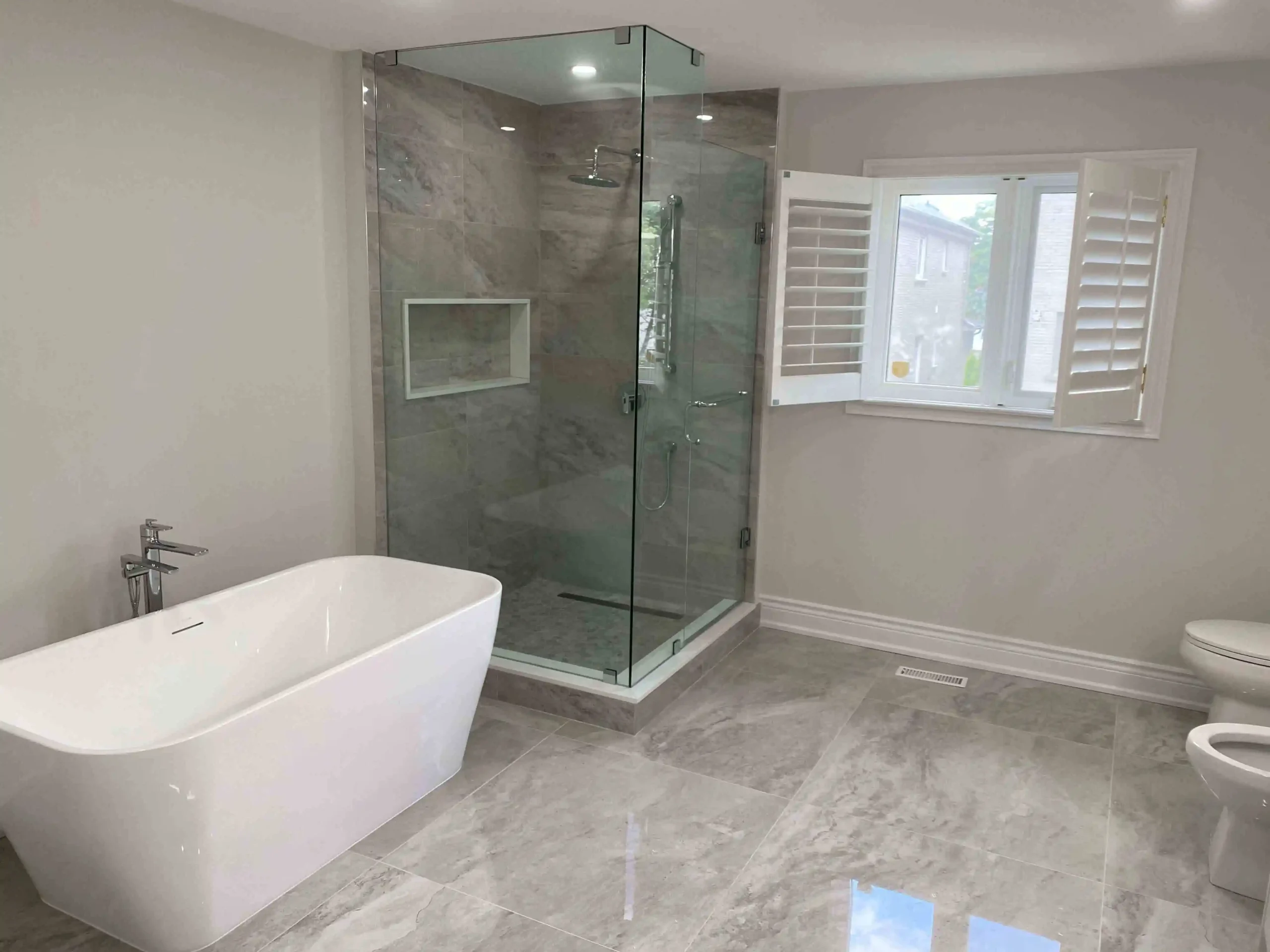 Contemporary bathroom with freestanding tub, glass shower, and marble tile in gta
