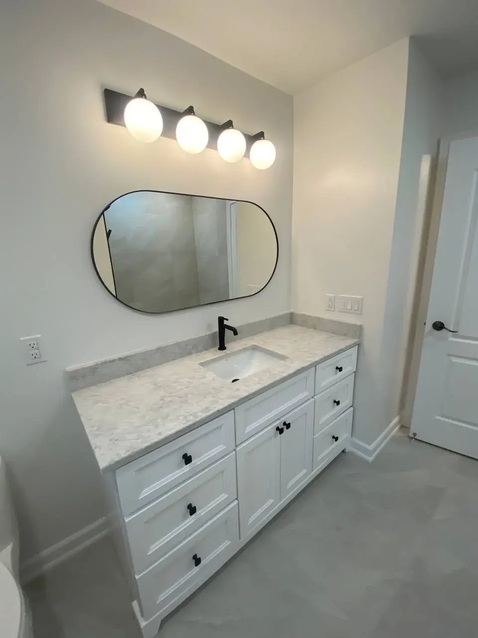 Minimalist bathroom vanity featuring white cabinetry, matte black faucet, oval mirror, and quartz countertop installed by RM Renovation